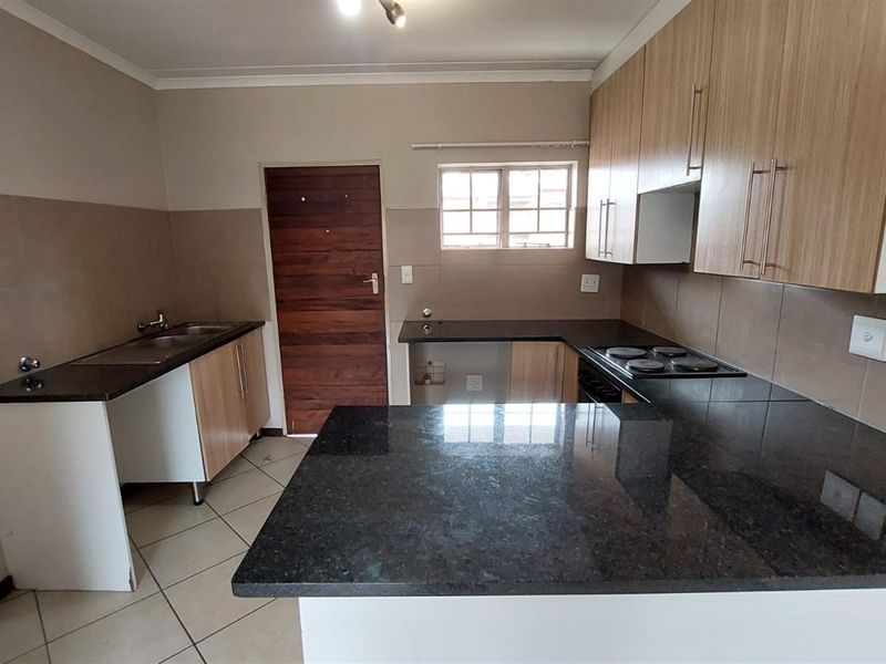 A functional kitchen featuring granite countertops, built-in cabinetry, an electric hob, and tiled flooring, offering a clean and practical workspace.
