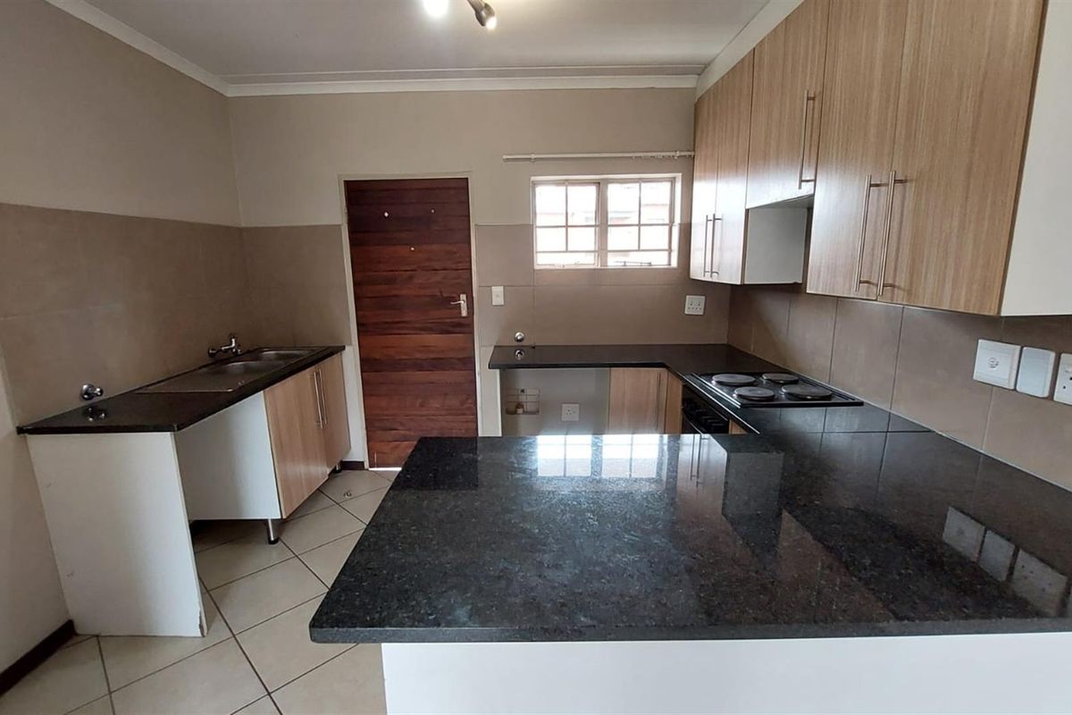 A functional kitchen featuring granite countertops, built-in cabinetry, an electric hob, and tiled flooring, offering a clean and practical workspace.