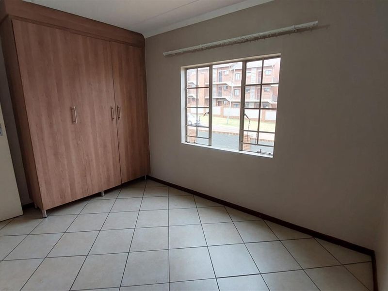 A vacant bedroom featuring tiled flooring, a built-in wooden wardrobe, and a window with security bars.