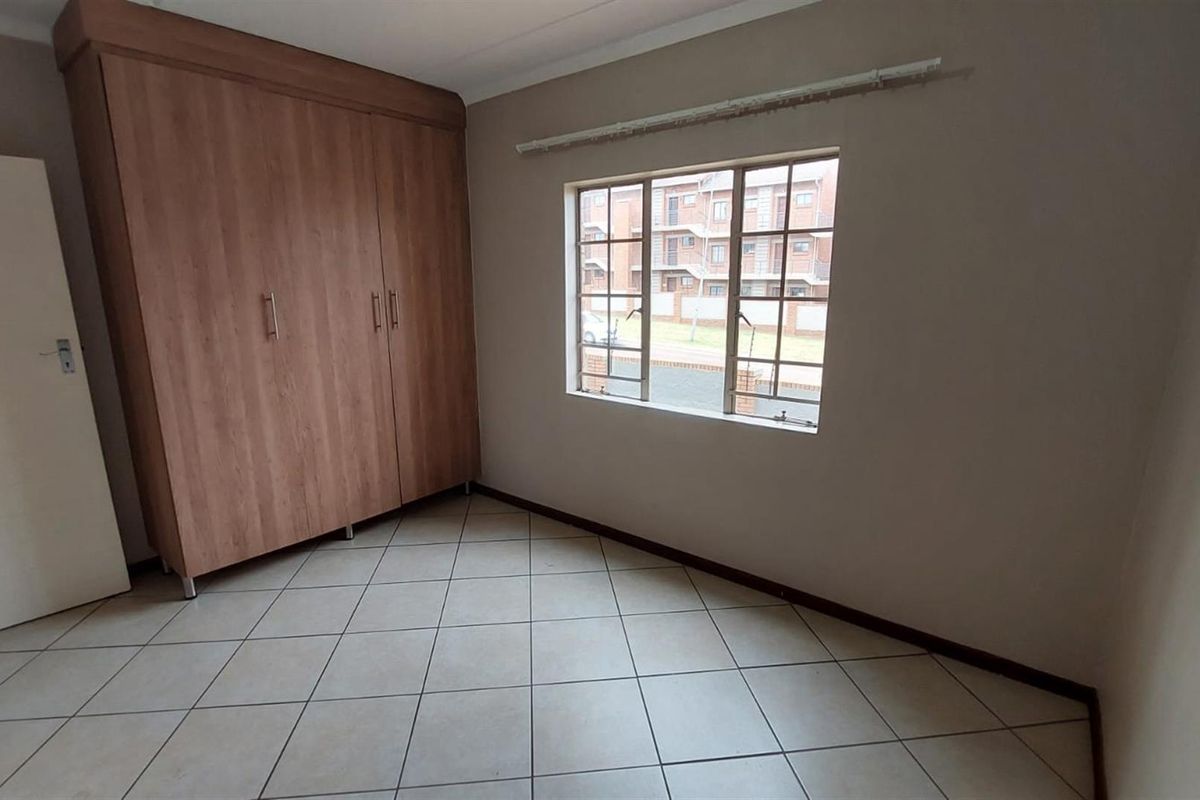 A vacant bedroom featuring tiled flooring, a built-in wooden wardrobe, and a window with security bars.