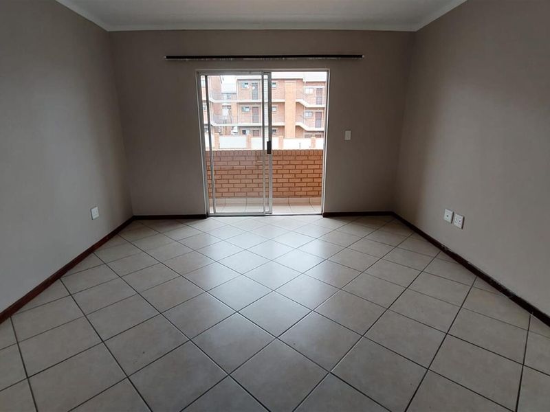 A spacious, empty living area featuring neutral tiled flooring and a sliding glass door providing access to an outdoor balcony.