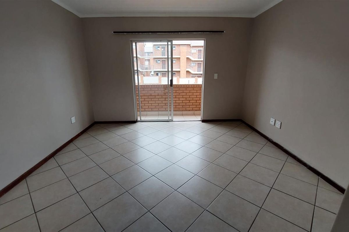 A spacious, empty living area featuring neutral tiled flooring and a sliding glass door providing access to an outdoor balcony.