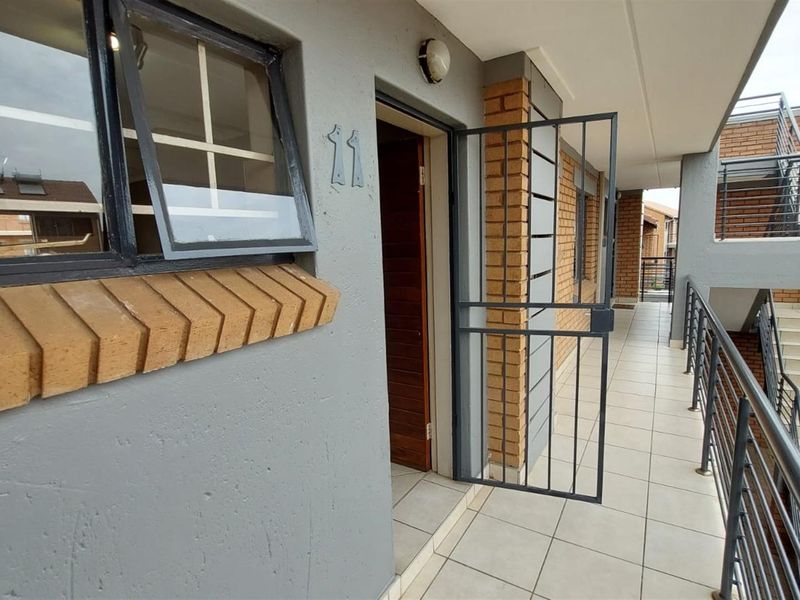 Exterior view of the unit entrance featuring a security gate, tiled walkway, and brick facade detailing in a townhouse complex.