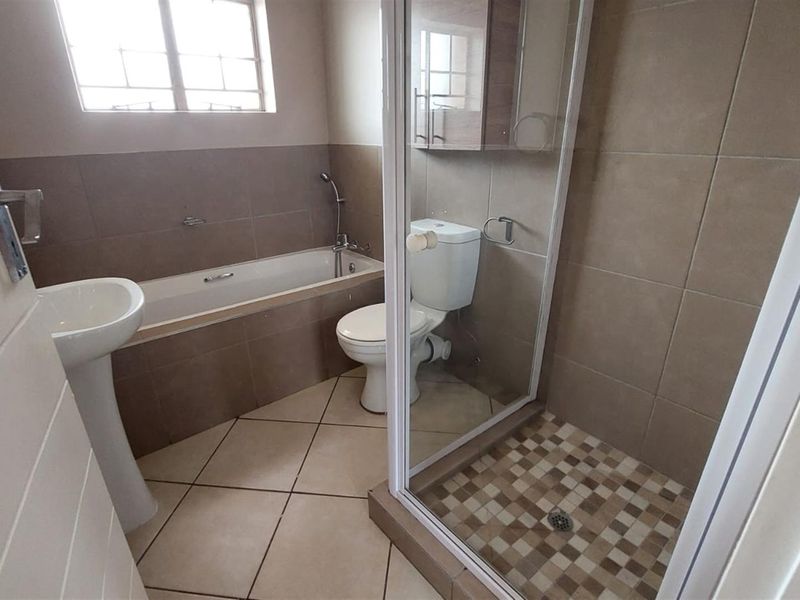 A functional bathroom featuring a pedestal basin, a built-in bathtub, a separate shower enclosure, and neutral wall and floor tiling.