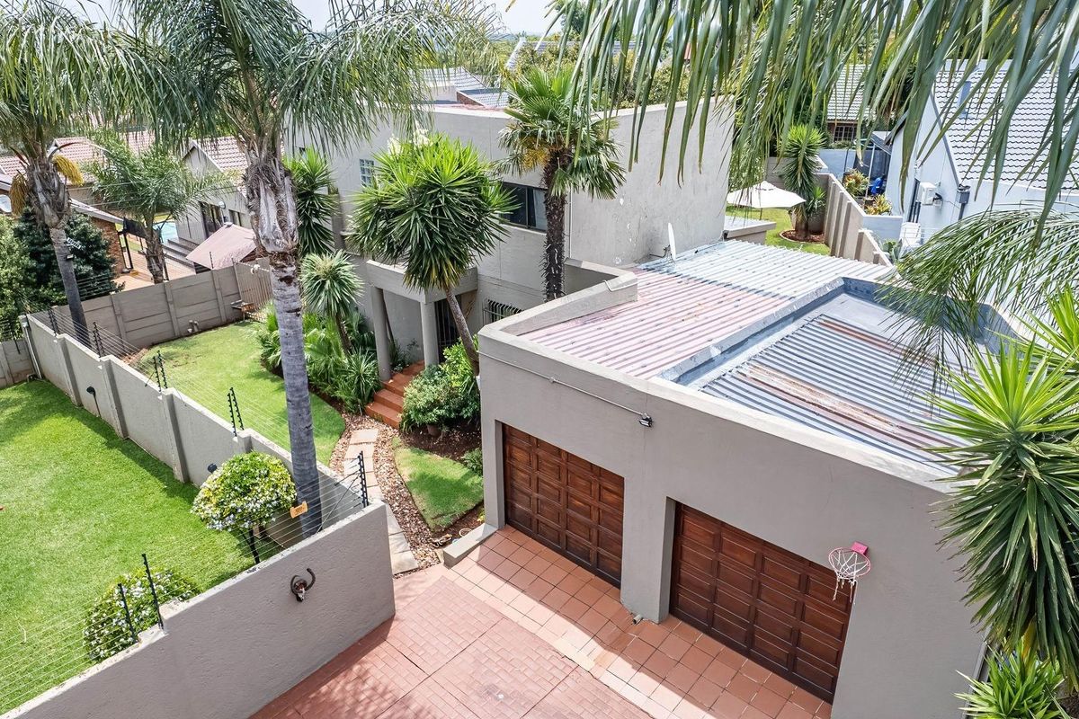 Aerial view of a residential property featuring a double garage, paved driveway, landscaped garden, and perimeter walling.