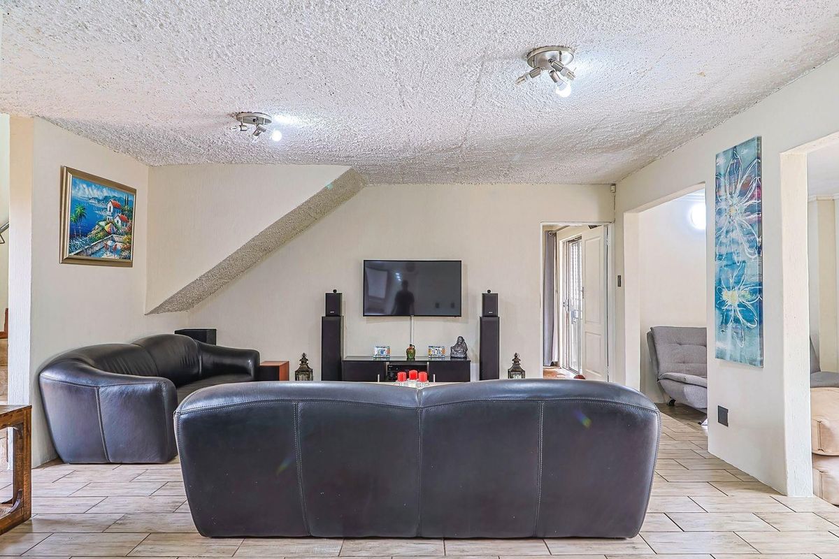 A spacious living room featuring tiled flooring, a textured ceiling, and a built-in staircase bulkhead, providing a functional and open living area.