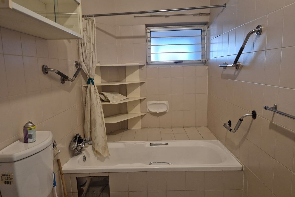 A functional bathroom featuring a bathtub with shower attachment, grab rails for accessibility, and built-in corner shelving.
