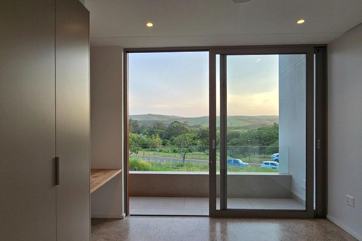 Modern bedroom featuring built-in cabinetry, a sleek desk area, and large sliding glass doors opening onto a private balcony with scenic landscape views.