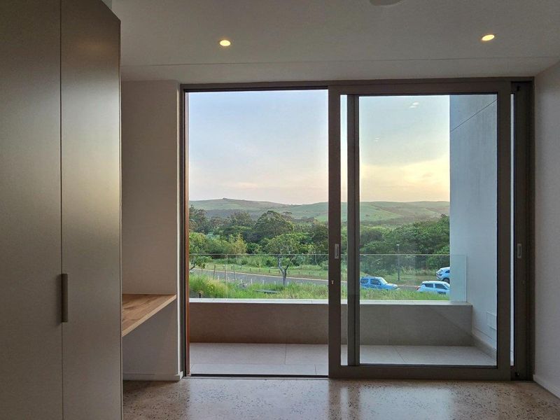Modern bedroom featuring built-in cabinetry, a sleek desk area, and large sliding glass doors opening onto a private balcony with scenic landscape views.