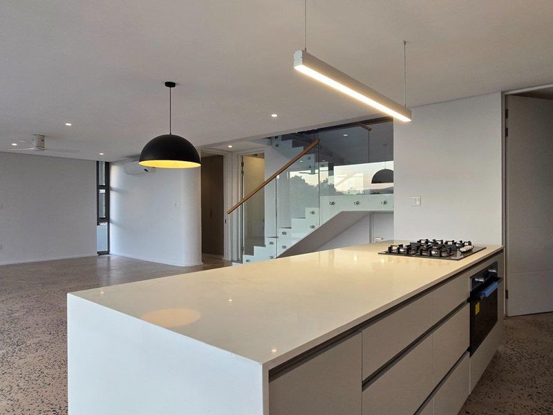 Modern open-plan living area featuring a sleek kitchen island with integrated cooktop, polished concrete flooring, and a contemporary glass-railed staircase.