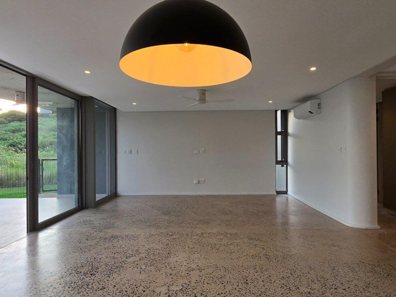 Spacious open-plan living area featuring polished concrete flooring, large sliding glass doors leading to a patio, and modern recessed lighting.