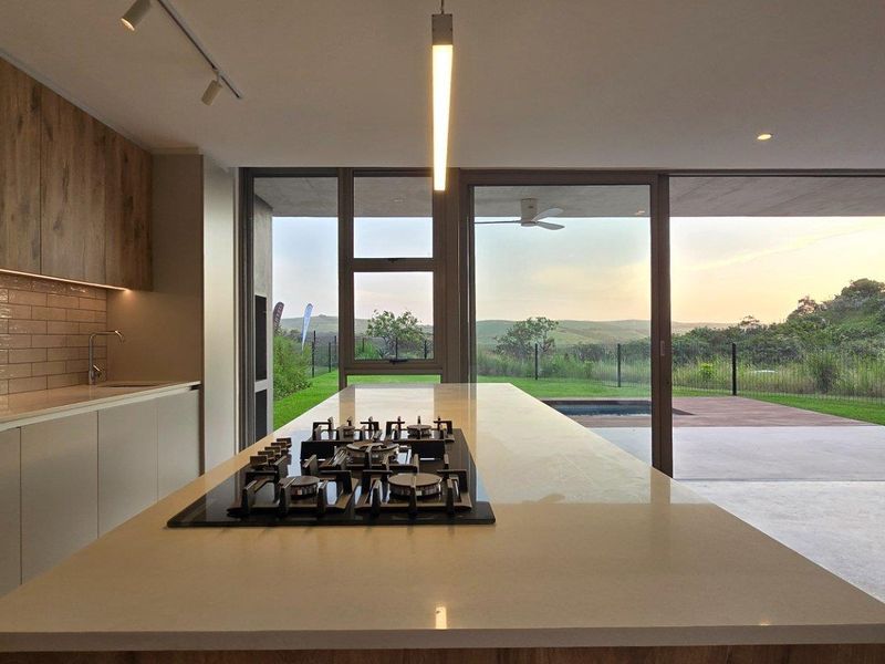 Modern open-plan kitchen featuring a large central island with integrated gas hob, sleek cabinetry, and seamless flow to the outdoor patio and garden.