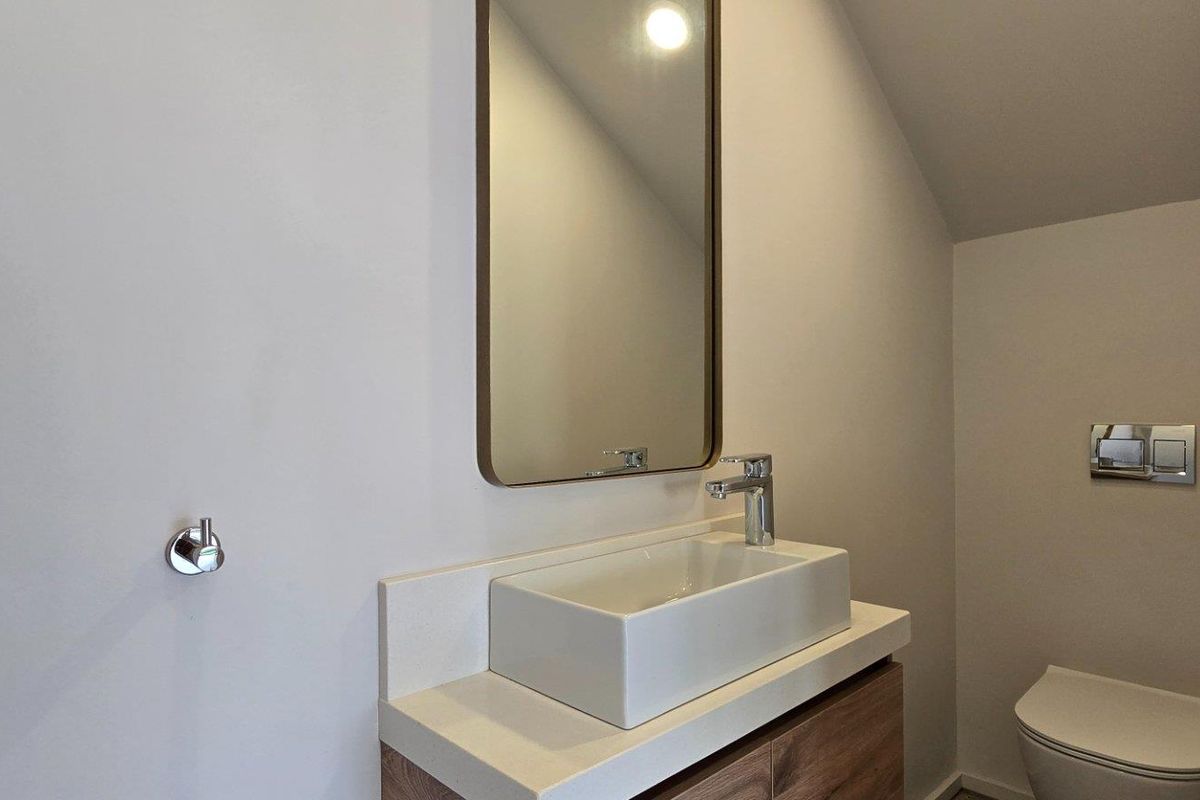 A modern bathroom featuring a sleek vanity with a vessel sink, wall-mounted mirror, and a concealed cistern toilet.