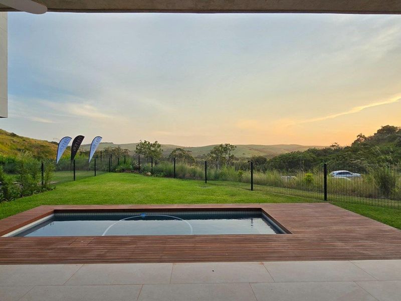 A well-maintained backyard featuring a swimming pool with timber decking, a manicured lawn, and scenic hillside views.