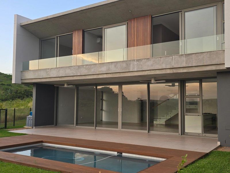 Modern double-story residence featuring a rear patio, swimming pool with timber decking, and large glass sliding doors opening to the interior living spaces.