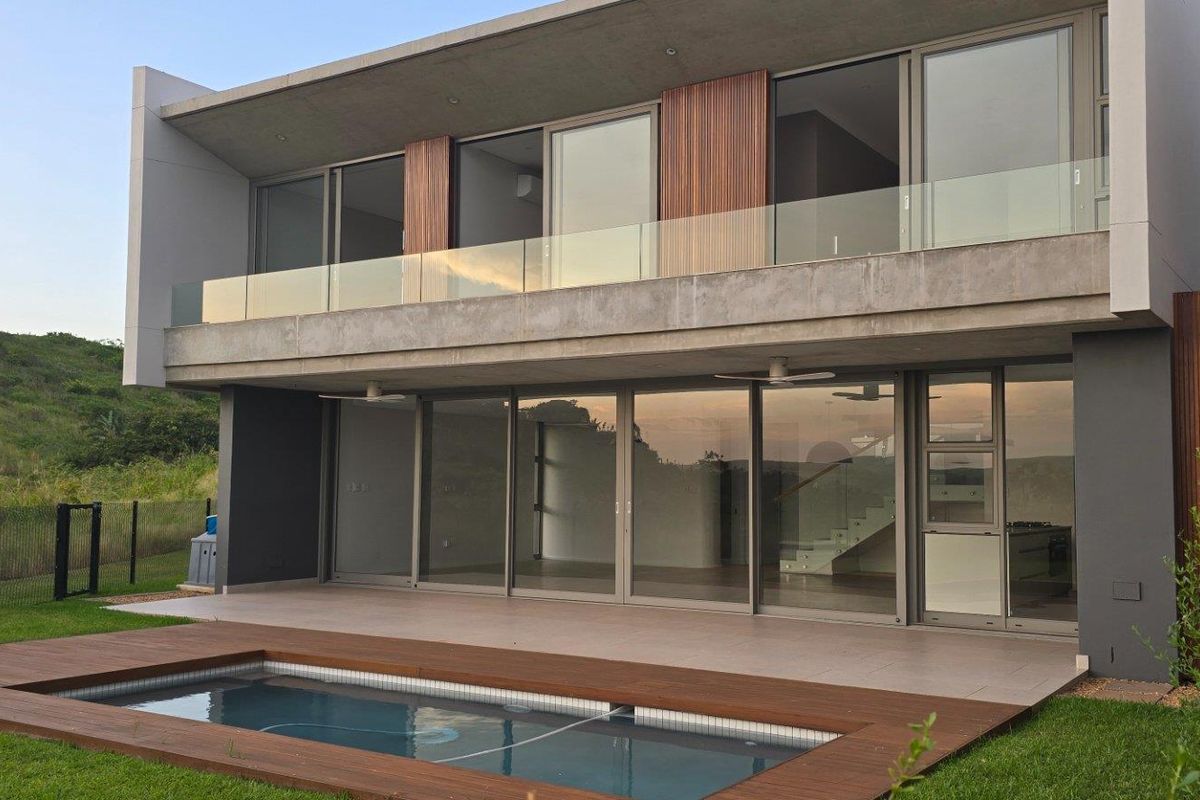 Modern double-story residence featuring a rear patio, swimming pool with timber decking, and large glass sliding doors opening to the interior living spaces.