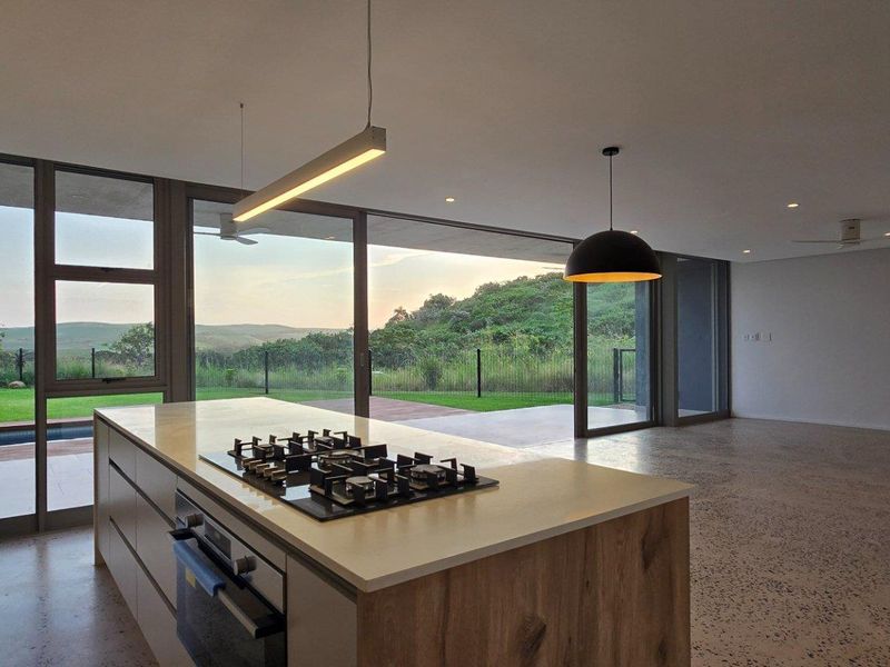 Modern open-plan kitchen and living area featuring a central island with built-in hob, polished concrete floors, and expansive sliding doors opening to a patio.