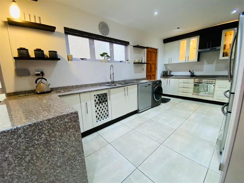 A well-maintained kitchen featuring granite countertops, white cabinetry, integrated oven and hob, and tiled flooring with a dedicated laundry appliance space.