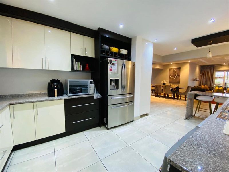 Modern open-plan kitchen featuring high-gloss cabinetry, granite countertops, and integrated storage, flowing seamlessly into the adjacent dining and living areas.