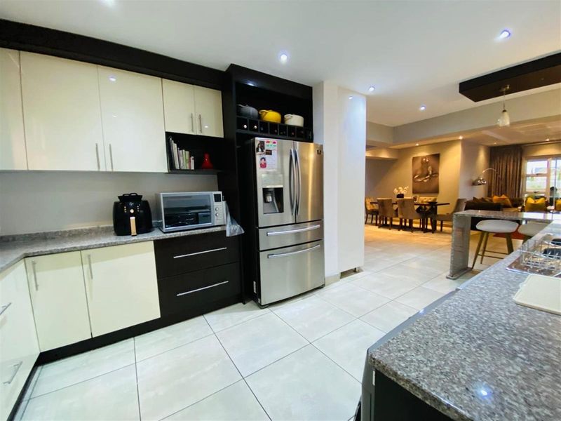Modern open-plan kitchen featuring high-gloss cabinetry, granite countertops, and integrated storage, flowing seamlessly into the adjacent dining and living areas.