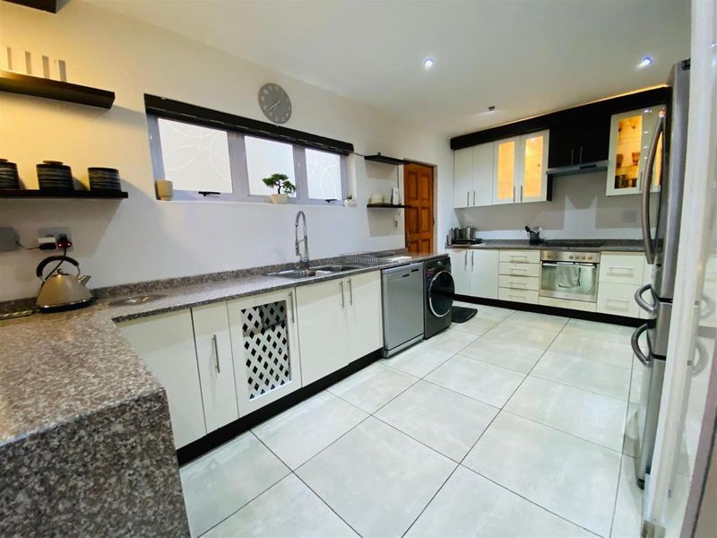 Modern kitchen featuring granite countertops, built-in cabinetry, integrated oven, hob, and extractor fan with tiled flooring and ample workspace.
