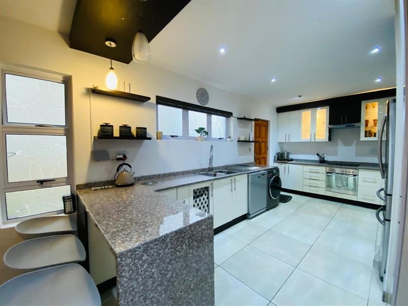 Modern kitchen featuring granite countertops, built-in cabinetry, integrated oven and hob, and a breakfast bar area with tiled flooring.