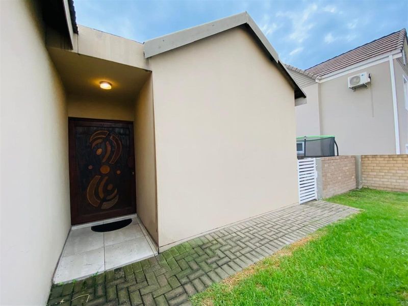 Exterior view of the home entrance featuring a covered porch, decorative wooden front door, and paved walkway leading to the garden area.