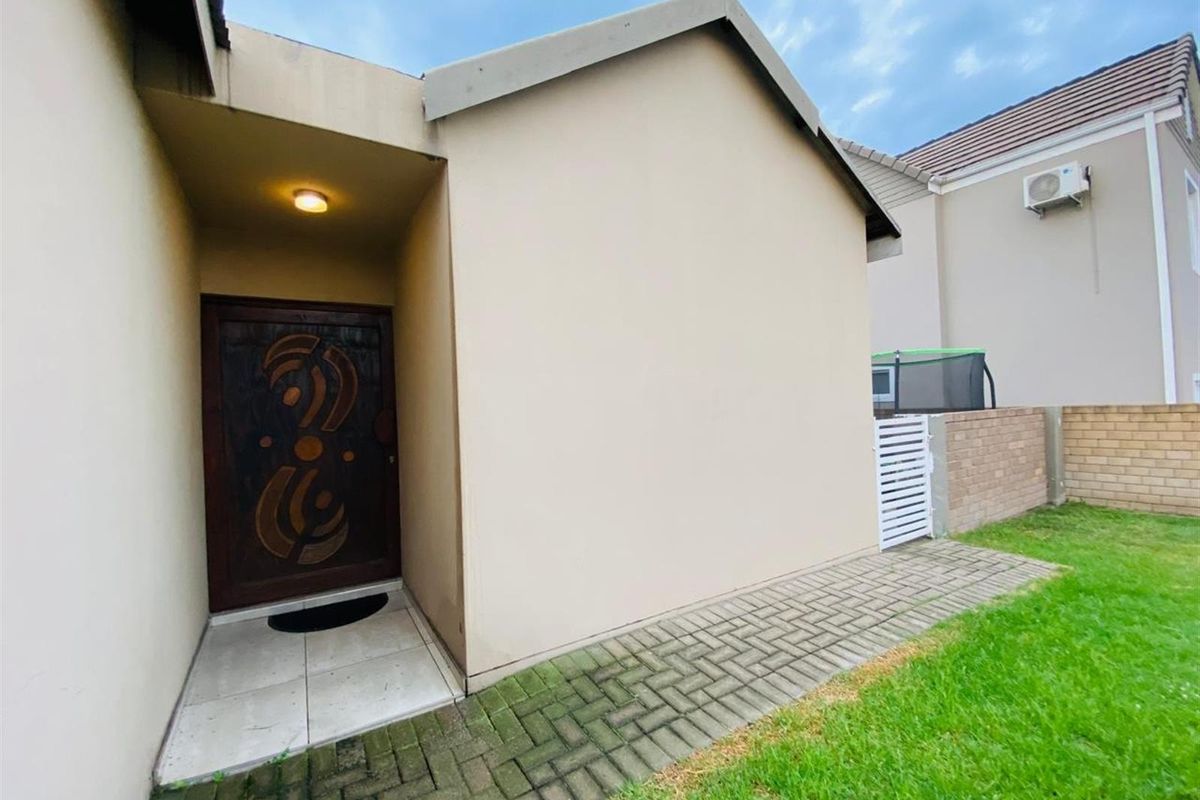Exterior view of the home entrance featuring a covered porch, decorative wooden front door, and paved walkway leading to the garden area.