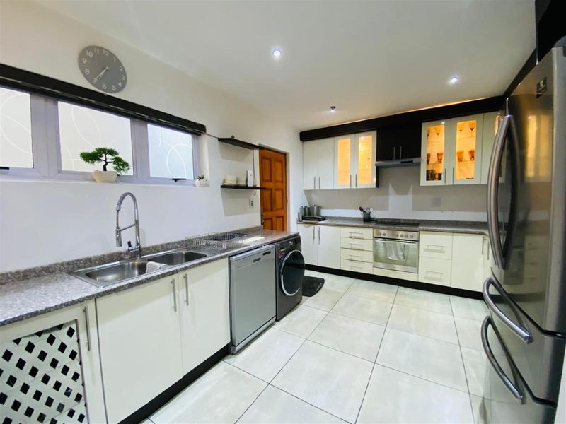 Modern kitchen featuring white cabinetry, granite countertops, stainless steel sink, built-in oven, hob, and extractor fan with tiled flooring.