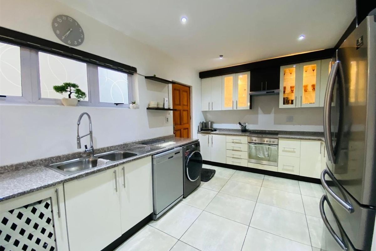 Modern kitchen featuring white cabinetry, granite countertops, stainless steel sink, built-in oven, hob, and extractor fan with tiled flooring.