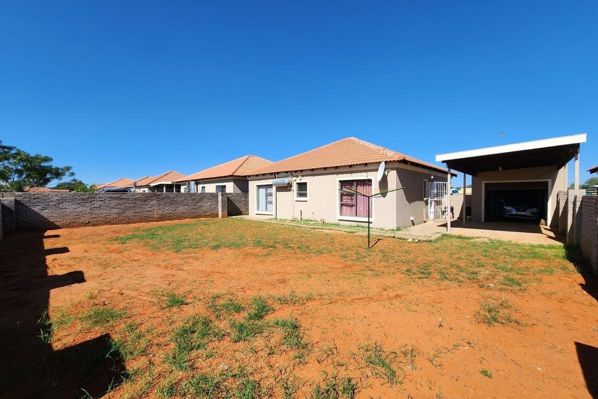 Rear view of the townhouse featuring a spacious backyard, perimeter brick wall, and an attached carport.