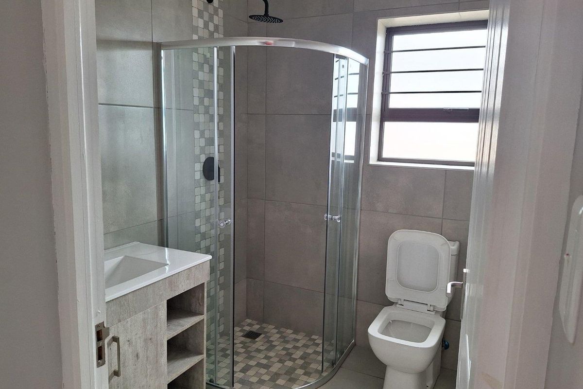 Modern bathroom featuring a corner glass shower enclosure, wall-mounted shower head, vanity basin with storage, and a standard toilet.