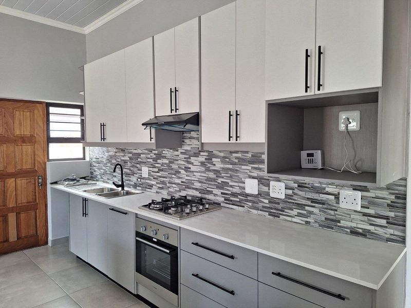 Modern kitchen featuring two-tone cabinetry, stone countertops, a built-in gas hob, electric oven, extractor fan, and a stylish mosaic tile backsplash.