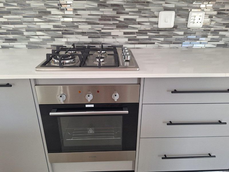 Modern kitchen featuring a built-in stainless steel oven, gas hob, stone countertop, and a decorative mosaic tile backsplash with contemporary cabinetry.