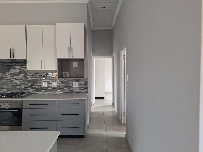 Modern kitchen featuring two-tone cabinetry, stone countertops, mosaic tile backsplash, and integrated oven with gas hob, leading into a tiled hallway.