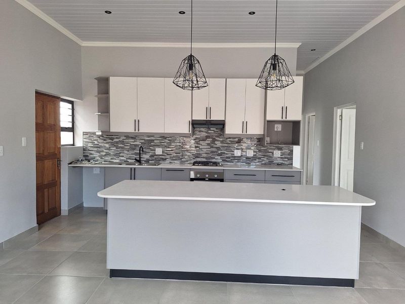 Modern kitchen featuring a central island, built-in cabinetry, mosaic tile backsplash, integrated oven and hob, and contemporary pendant lighting.