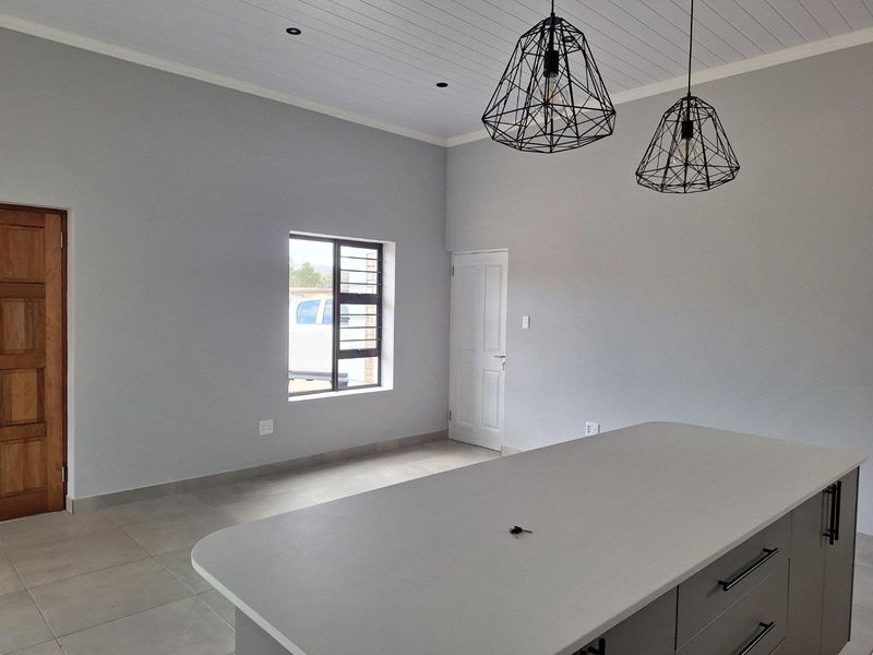 Modern open-plan kitchen area featuring a central island with stone countertop, tiled flooring, and contemporary pendant lighting.