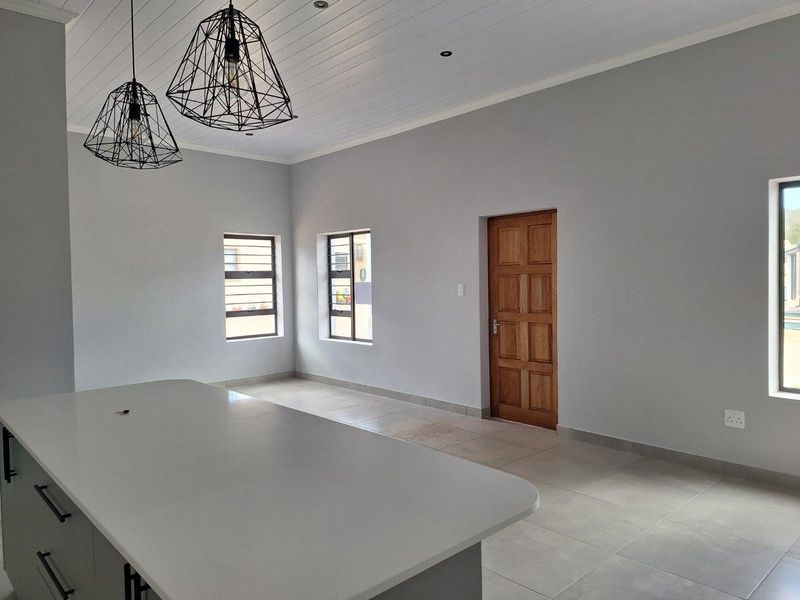 A bright, modern open-plan living area featuring tiled flooring, a central kitchen island, and a classic wooden door.