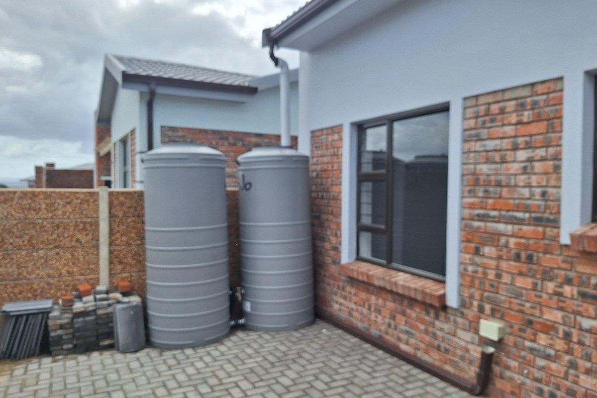 Exterior view of the property featuring two large grey water storage tanks installed against a brick facade with paved ground area.