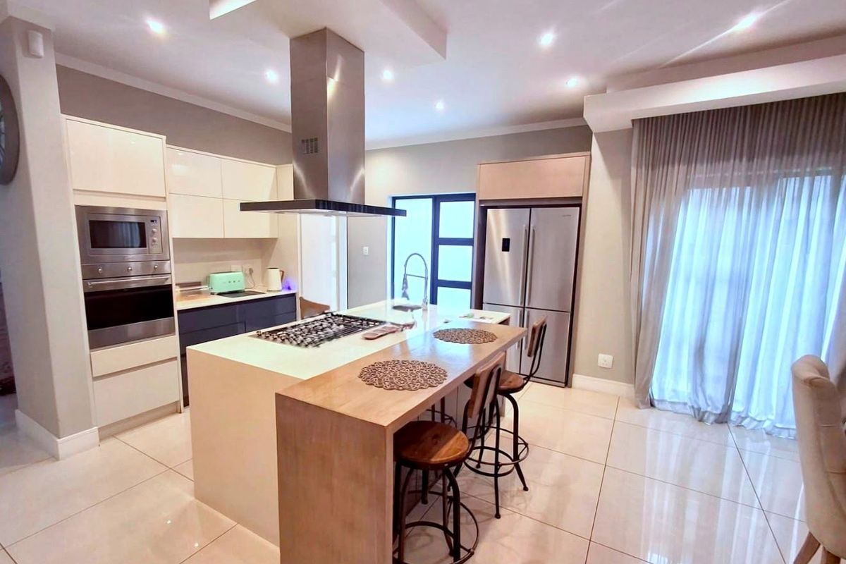 Modern kitchen featuring a central island with gas hob, integrated appliances, sleek cabinetry, and polished tiled flooring with recessed lighting.