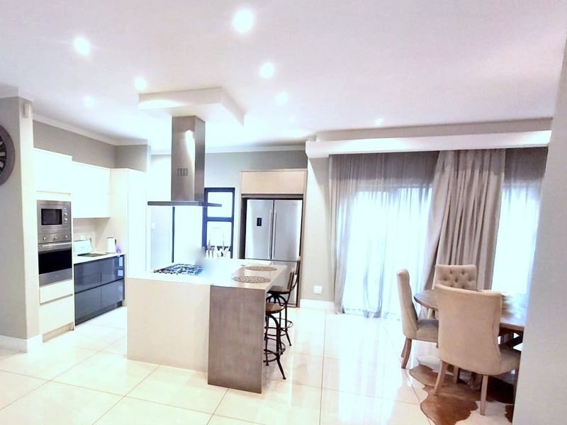 Modern open-plan kitchen featuring a central island with gas hob, built-in appliances, and sleek cabinetry, flowing into a bright dining area with sliding doors.