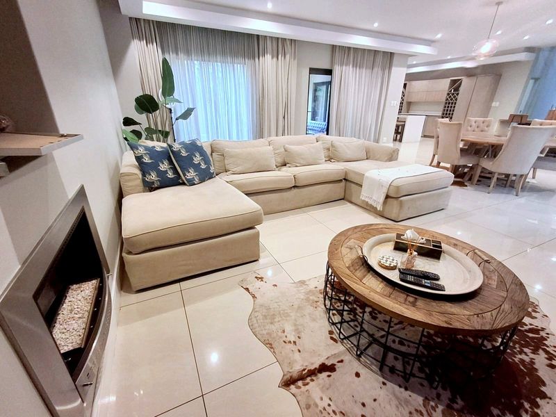 Spacious open-plan living and dining area featuring polished floor tiles, recessed lighting, and a modern built-in fireplace, seamlessly connected to the kitchen.