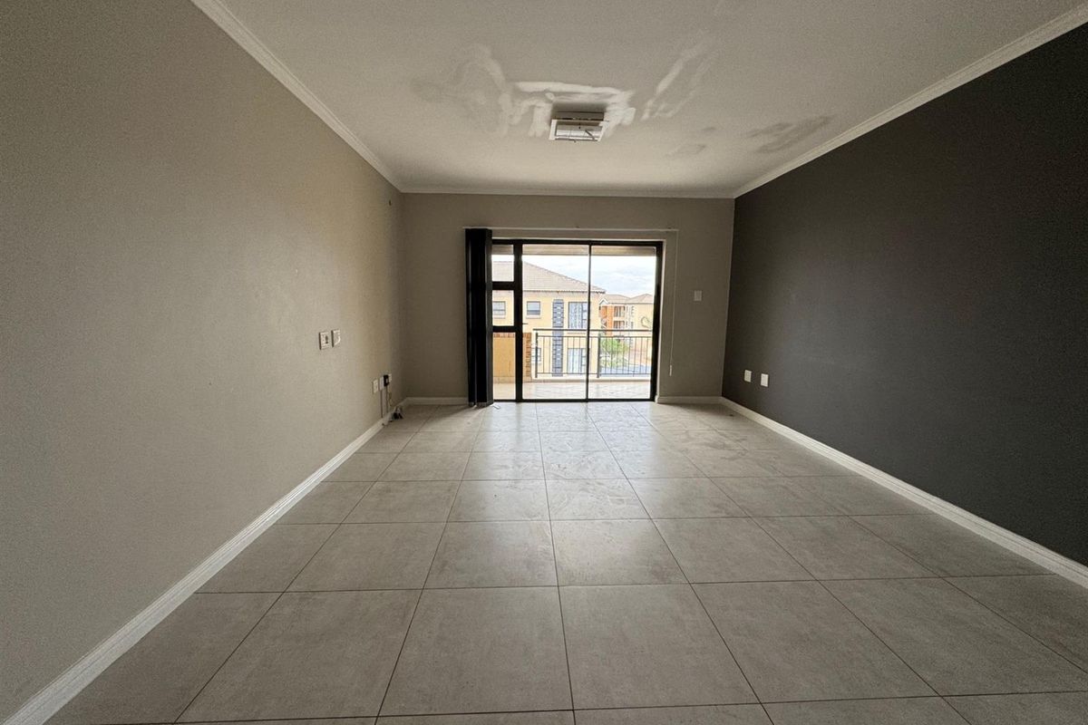 An empty living area featuring large format floor tiles, a dark accent wall, and sliding glass doors leading to a balcony.