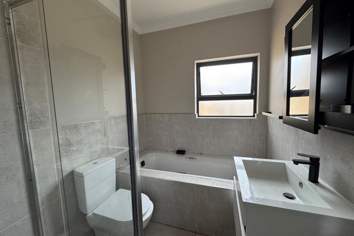 A modern bathroom featuring a built-in bathtub, a glass-enclosed shower, a contemporary vanity with a basin, and neutral wall tiling.