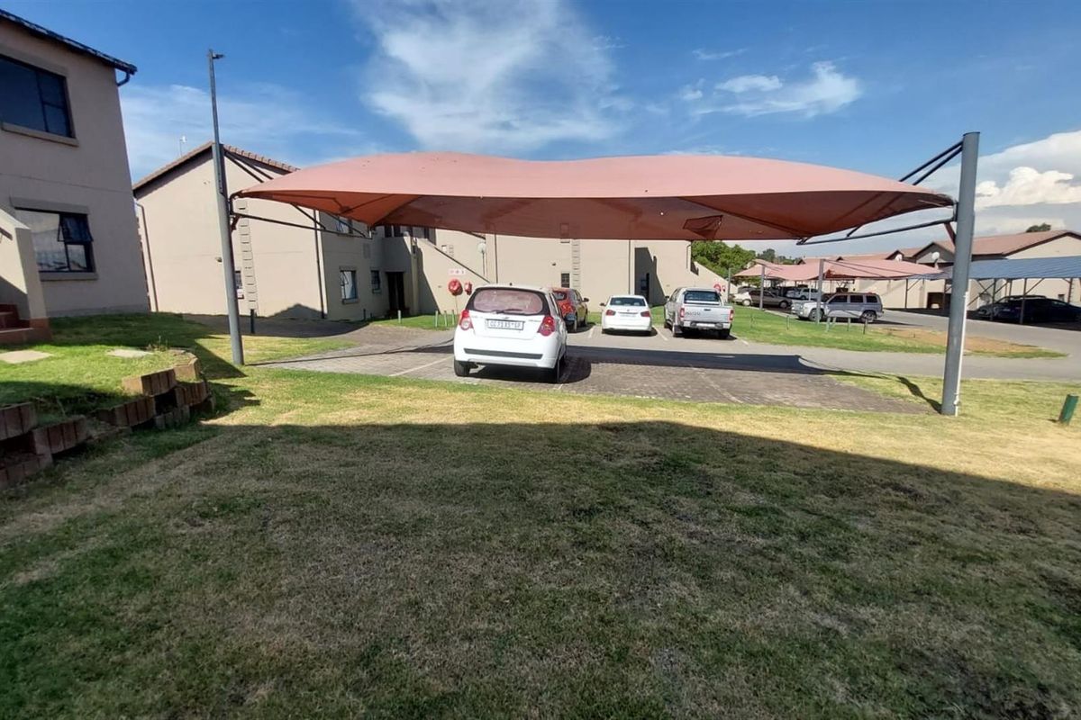 Rear exterior view of the townhouse complex featuring a paved parking area with shade cloth carports and a shared lawn space.