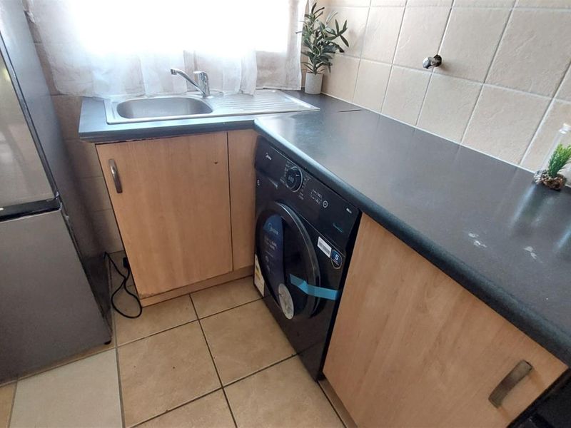 A functional laundry area featuring laminate cabinetry, a dark countertop, stainless steel sink, and tiled finishes.