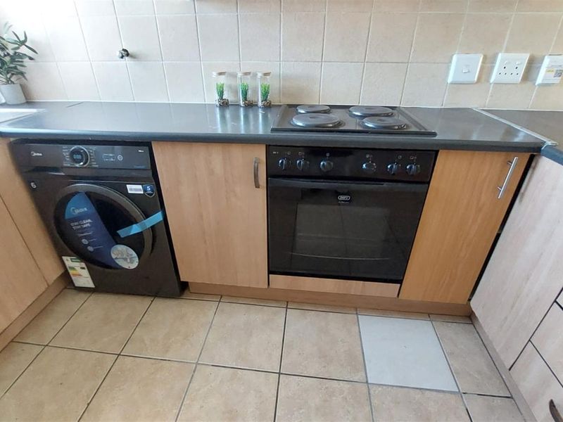 A functional kitchen featuring light wood-finish cabinetry, dark laminate countertops, a built-in oven with electric hob, and tiled flooring.