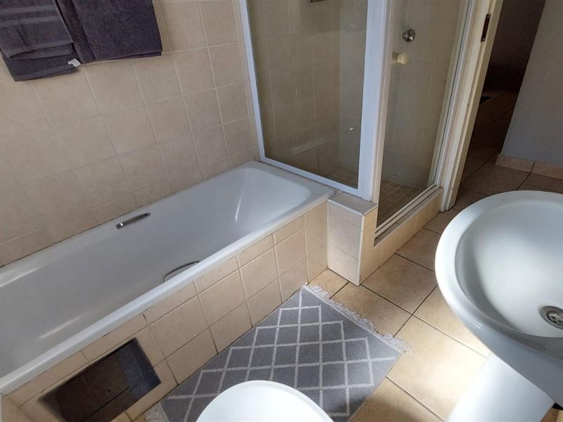 A functional bathroom featuring a bathtub, separate shower enclosure, and a pedestal basin with neutral ceramic tiling throughout.
