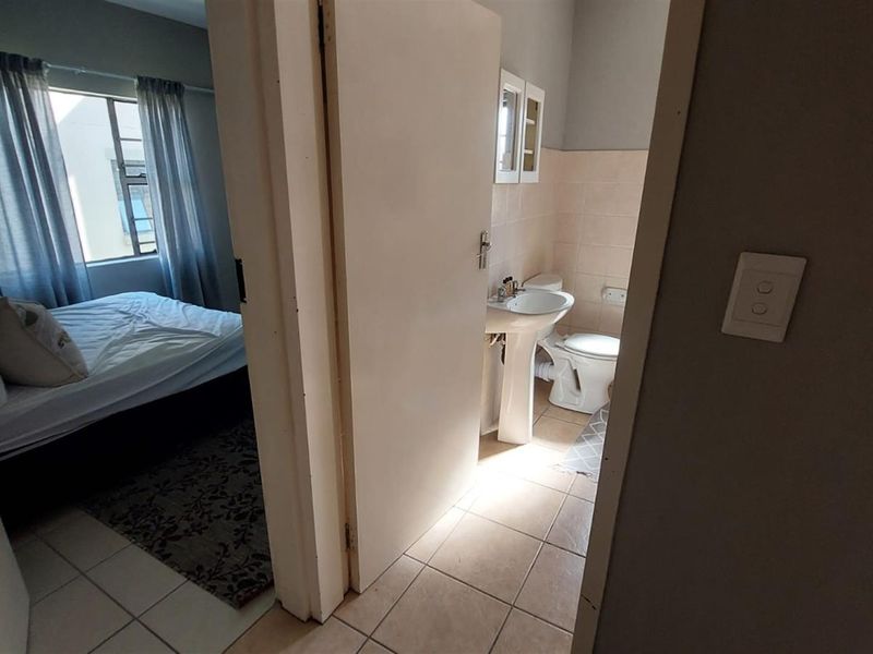 A view from the hallway into a bedroom with an en-suite bathroom featuring a pedestal basin and toilet.