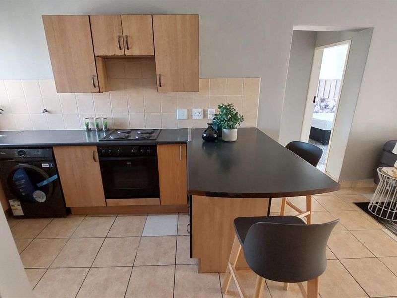 Open-plan kitchen featuring wood-finish cabinetry, dark laminate countertops, built-in oven and hob, and a breakfast bar, seamlessly connecting to the living area.